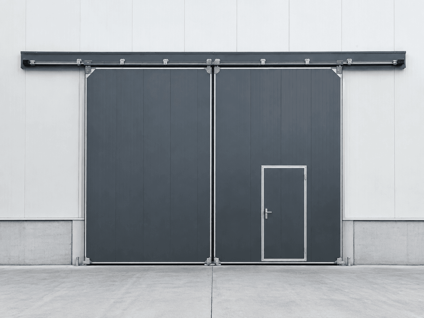 Graphite industrial sliding door with overhead track and integrated personnel door
